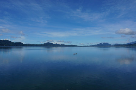 A boat in the middle of a very shady lake, with shades of blue all around.の写真素材