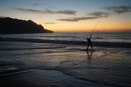 Fisherman casting in ocean at sunsetの写真素材