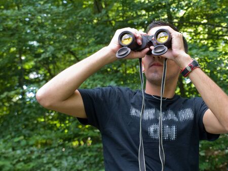 Young man looking through binoculars while hiking out in nature