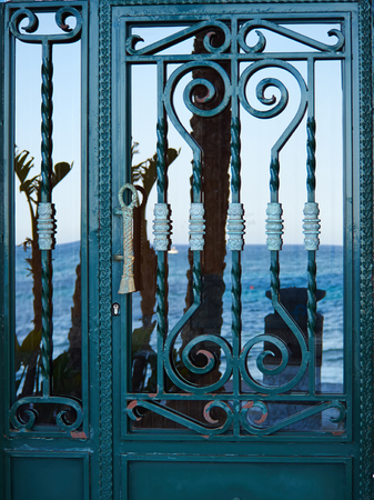 Old vintage Spanish style decorative wrought iron door with the ocean reflected on the glassの写真素材