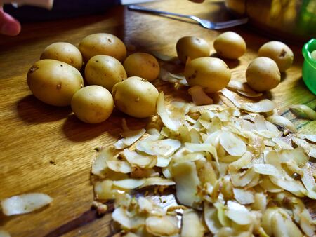 Peeling fresh organic potatoes on a rustic wooden kitchen surface boardの写真素材