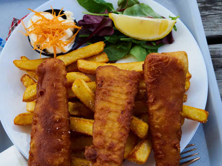 Traditional Classical British quisine dish fish and chips served with potato, lemon and dressing