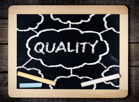 Quality handwritten with white chalk on a blackboard on wood background の写真素材