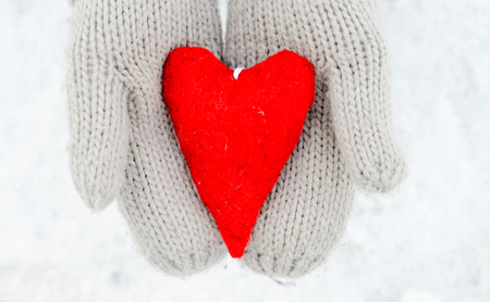 Hands in gloves holding red heartの写真素材