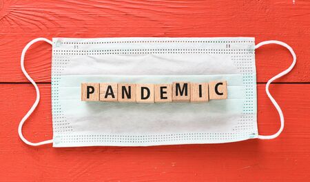 PANDEMIC. The word pandemic arranged from wooden letters on a protective mask and a red table.の写真素材