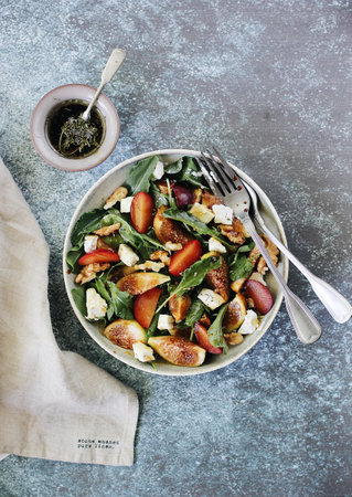 Salad with figs, tomatoes, nuts, cheese, greens, plums and sprinkled with honeyの写真素材