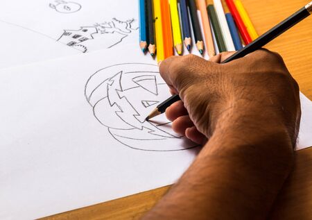 Hand of man drawing pumpkin of Halloween by pencil.