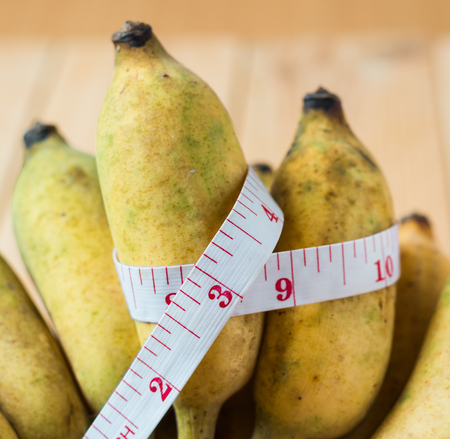 Banana with measure tape on wooden table  for healthy lifestyle diet concept.の写真素材