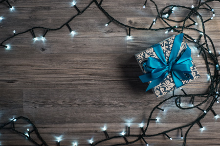 Christmas gift box with blue bow and bokeh lights on wooden surfaceの写真素材