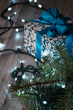 Christmas gift box with blue bow and bokeh lights on wooden surfaceの写真素材