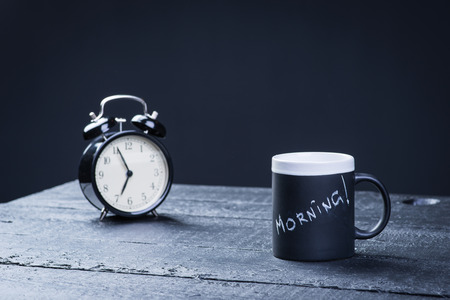 Black tea cup with alarm clock on wooden tableの写真素材