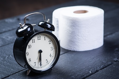 Alarm clock with toilet paper on a black wooden tableの写真素材