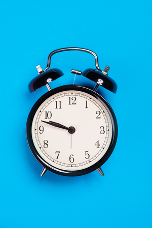 Old vintage alarm clock standing on the blue paper surfaceの写真素材