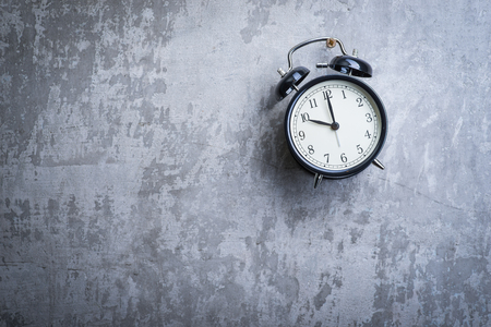 Unusual picture of old vintage alarm clock hanging on the grey concrete wallの写真素材