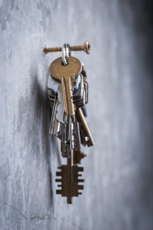 A bunch of old worn keys hanging on the screw on the grey concrete wallの写真素材