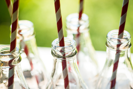 Glass cocktail bottles with straws over the green sunny backgroundの写真素材