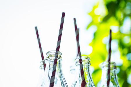 Glass cocktail bottles with straws over the green sunny backgroundの写真素材