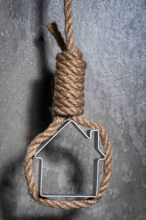 Small house framed with hangman's noose hanging over the grey concrete wall