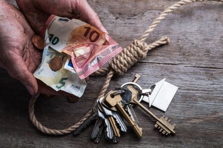 Hands holding money with hangman's noose, keys and money on brown wooden background
