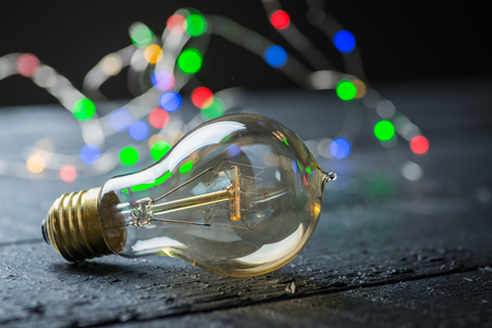 Vintage tungsten bulb on a black wooden table with colorful lights at the backgroundの写真素材