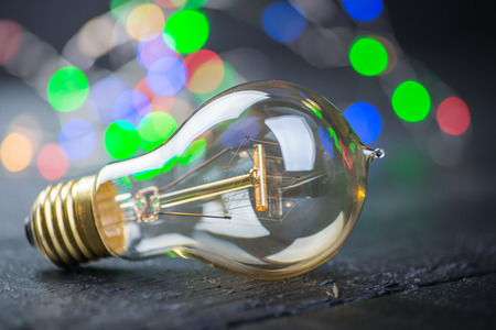 Vintage tungsten bulb on a black wooden table with colorful lights at the backgroundの写真素材