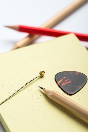 Yellow notepad with three pencils, string and mediator on white surfaceの写真素材