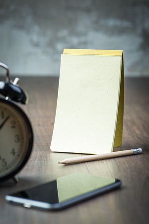 Black vintage alarm clock with notepad and phoneの写真素材