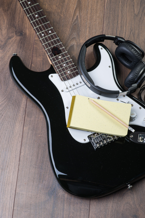 Electric guitar with headphones, notedpad and pencil on a brown wooden floorの写真素材