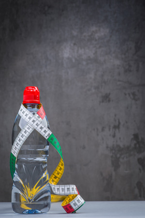 Bottle of fresh still water with measuring tape over grey wallの写真素材
