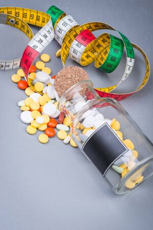 A bottle of diet pills with measuring tape on greyの写真素材