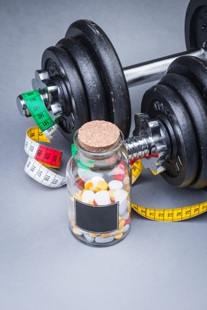 Heavy classical dumbbells with measuring tape and pills on grey surfaceの写真素材