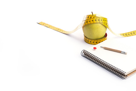 Fresh and green organic apple with metering tape and notebook over white backgroundの写真素材