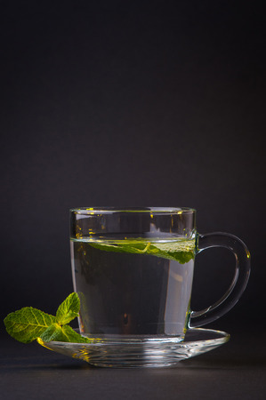 A cup of green and mint tea over black backgroundの写真素材