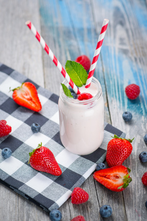 Jar with drinking yogurt, berries and straw on rustic wooden tableの写真素材