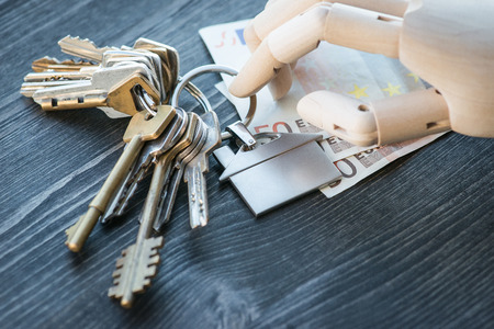 Artificial wooden hand holding the keys and money, on a rustic wooden table