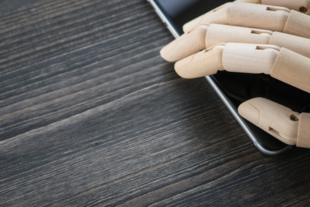 Artificial wooden hand with modern phone on wooden table