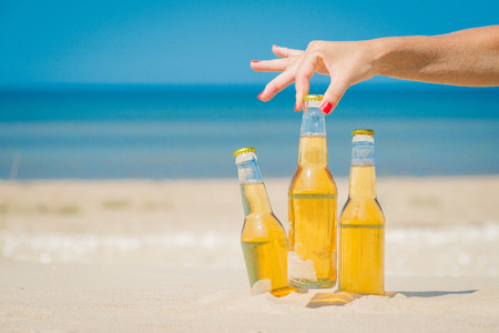 Ice cold beer bottles in the sand under the bright sunの写真素材