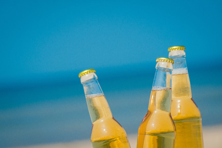 Ice cold beer bottles in the sand under the bright sunの写真素材