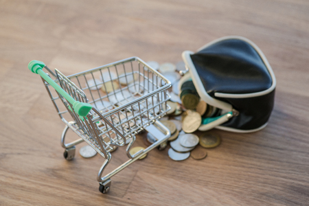 Shopping cart with wallet and coins on the wooden surfaceの写真素材