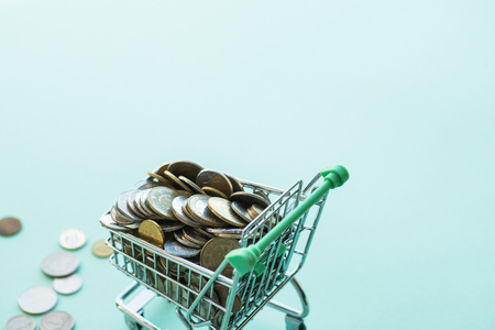 Shopping cart full of coins over the light green backgroundの写真素材