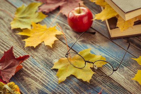 Eye glasses with book and autumn leaves on wooden tableの写真素材
