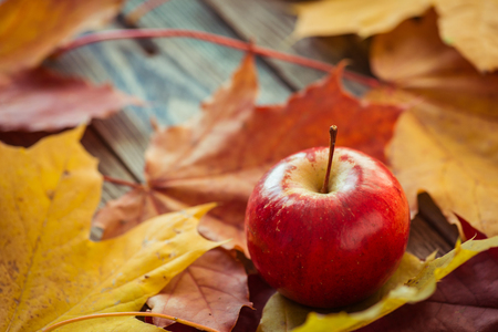 Red autumn apples with fallen leaves on wooden tableの写真素材