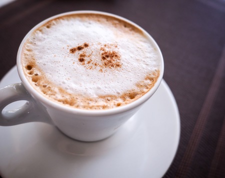 a whit cup of cappuccino coffee with cacao topping on wooden table background