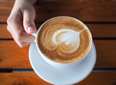 Woman's hand holding a cup of coffee on wood table, lift up a cup of coffee for drinkの写真素材