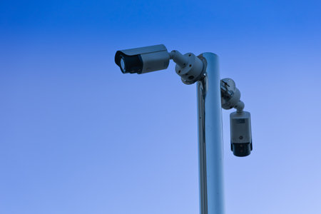 Two security cameras are mounted on a tall white pole, facing different directions. The image...
