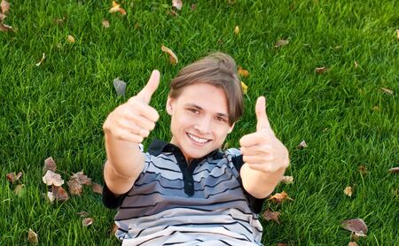 Young man lying on the grass with thumbs upの写真素材