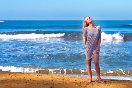 A young beautiful blond girl is staying near the ocean in the morningの写真素材