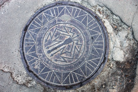 Manhole with metal cover in the cracked asphalt surfaceの写真素材