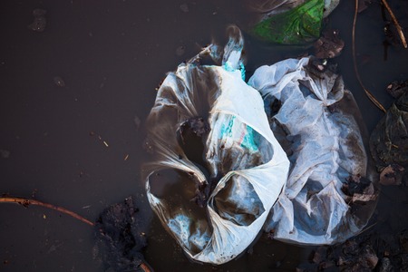 Thrown away plastic bags floating in black dirty water