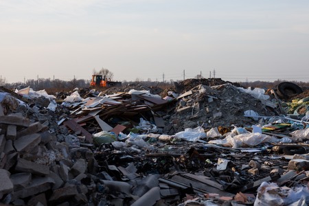 Piles of garbage on the landfill near the city with the bulldozer working in the distance